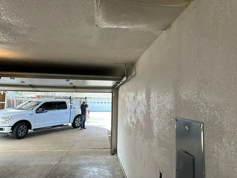 A white truck is parked in a garage next to a wall.