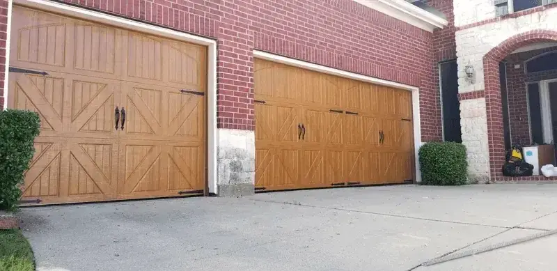 Two wooden garage doors are sitting in front of a brick building.