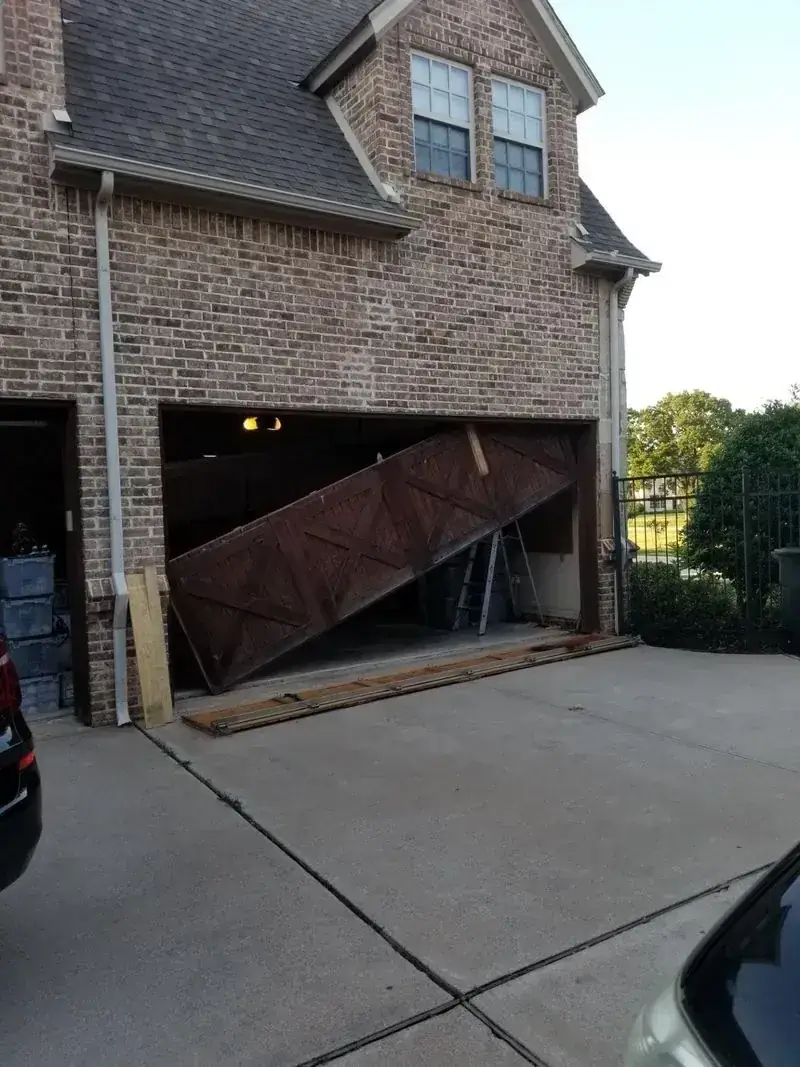 A car is parked in front of a brick house with a broken garage door.