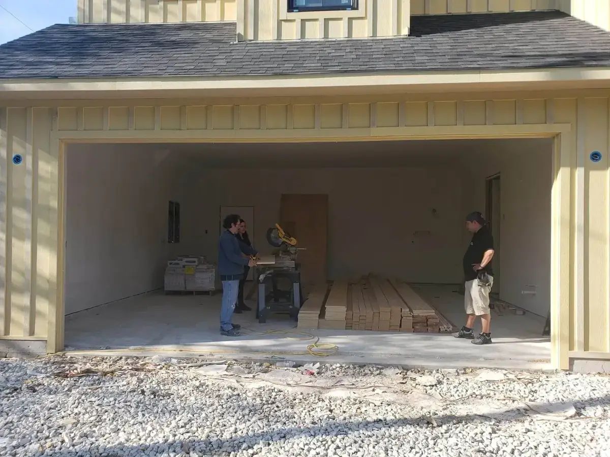 Two men are standing in front of a garage door that is open.